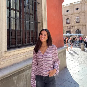 chica posando en la calle con una blusa de escote pico en estampados lila y lúrex y pantalón tejano gris oscuro