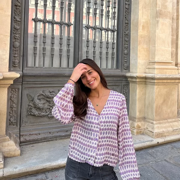 chica posando en la calle con una blusa de escote pico en estampados lila y lúrex y pantalón tejano gris oscuro