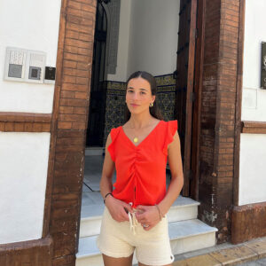 chica delante de una puerta abierta de un edificio con una blusa de manga corta en color coral y un short de tricotosa en crudo