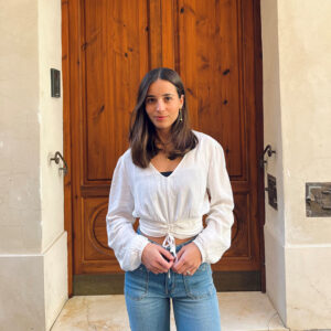 chica delante de una puerta marrón con blusa blanca con lurex plata, con fruncido en pieza frontal de cintura