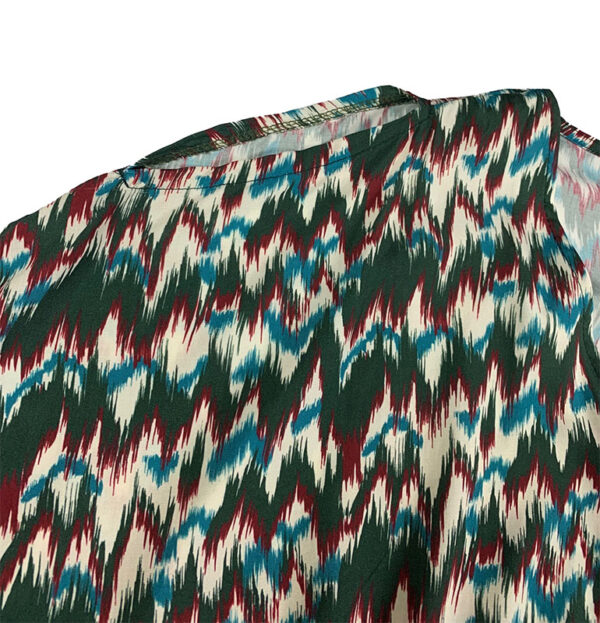 Detalle de la abertura en hombros de la blusa corta blanca con estampado verde, burdeos y turquesa con mangas murciélago y escote pico.