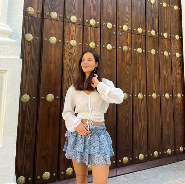 chica delante de portón de madera con una blusa blanca con lúrex plata y falda pantalón de gasa azul estampada con lúrex plata