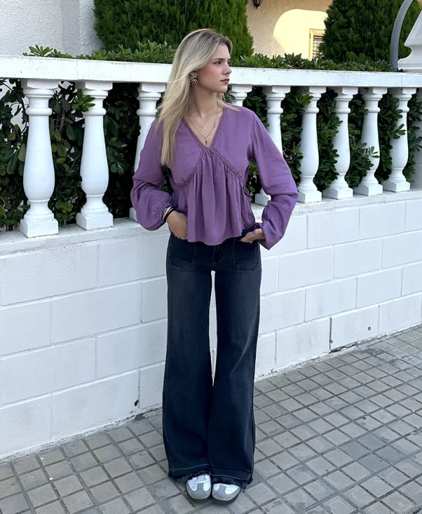 chica posando en la calle con un pantalón campana gris oscuro con dos bolsillos frontales y blusa rosa de escote pico con intersecciones con cuello