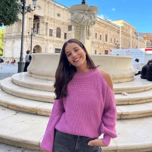 chica posando en la calle con un jersey rosa con el hombro izquierdo descubierto