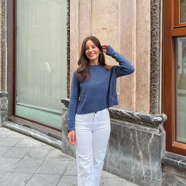 chica posando con un jersey azul con el hombro izquierdo descubierto y pantalón blanco