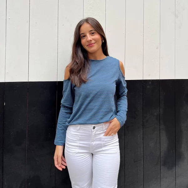 chica posando con una camiseta de rayas finas de color azul y gris antracita con los hombros descubiertos y mangas largas con un pantalón blanco