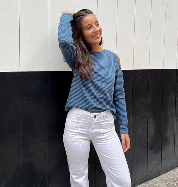 chica posando con una camiseta de rayas finas de color azul y gris antracita con los hombros descubiertos y mangas largas con un pantalón blanco