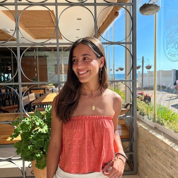 chica en un restaurante de playa con un top palabra de honor naranja con goma elástica en interior de escote y círculos de hilos plateados y dorados