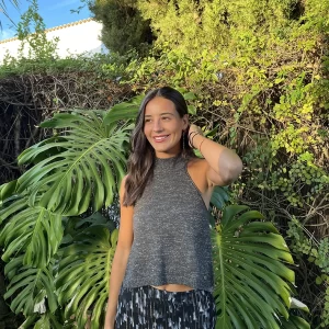 chica sonriendo delante de arbustos con una mano en el pelo con un top halter gris con hilo de lúrex plateado