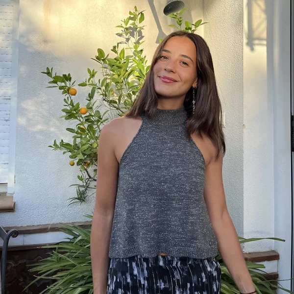 chica sonriendo delante de arbustos con una mano en el pelo con un top halter gris con hilo de lúrex plateado